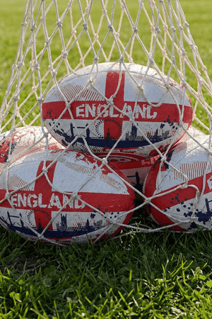 White and red Optimum England rugby balls with St George's cross and ENGLAND print in a net bag on grass - Optimum