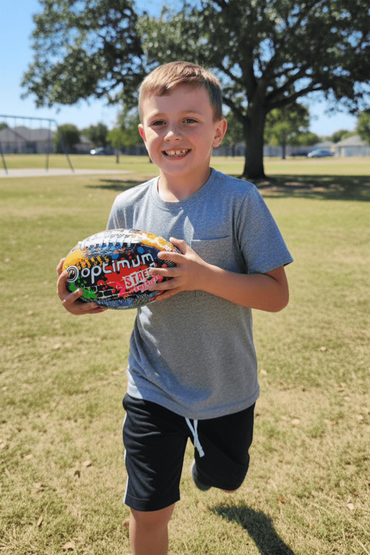 Young boy in a park holding the multicoloured Optimum Street American football - Optimum