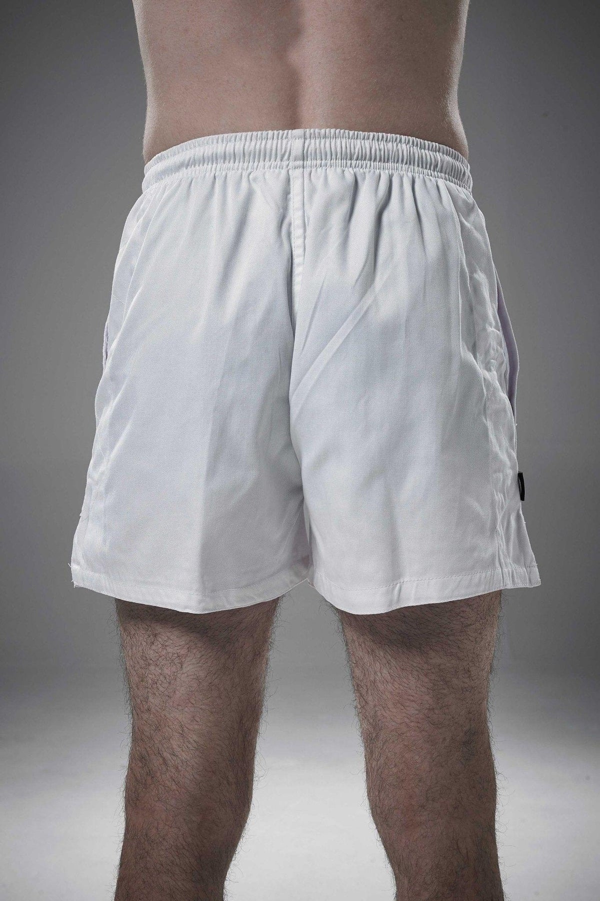 White Optimum rugby shorts worn by a man, rear view showing elasticated waistband, on grey studio background - Optimum